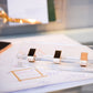 Close-up of Russell & Hazel's Acrylic Signature Hole Punch with three gold-toned clips on a desk, elegantly holding handwritten notes and adding a personal touch to the setup.