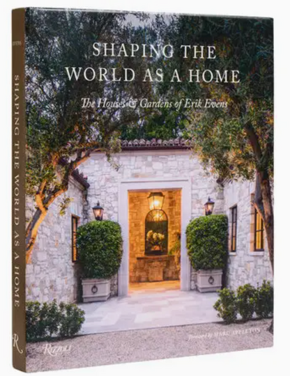 Book cover of “Shaping the World As A Home” by Rizzoli, showcasing a stone house with a wooden door and two potted plants by the entrance, elegantly reflecting California architecture blended with traditional design elements.