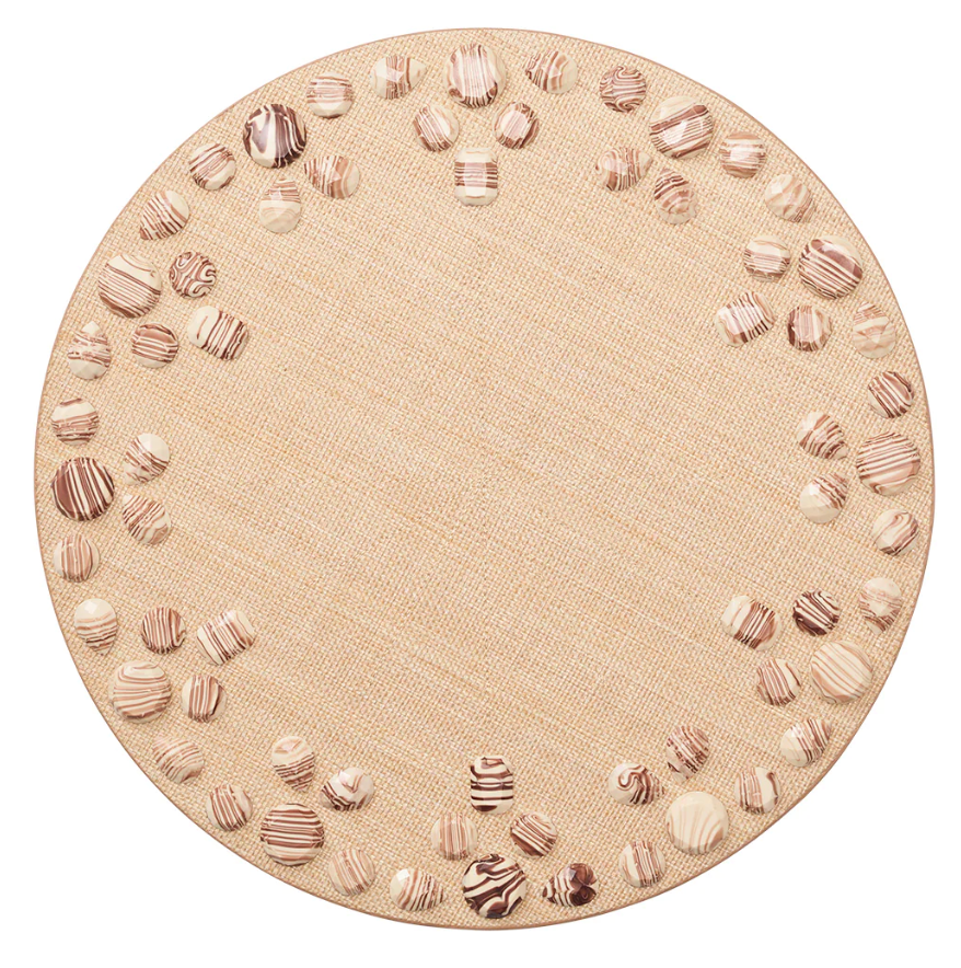 The Kim Seybert Cabochon Natural & Brown Placemat is a round beige mat with two concentric circles at the edge, adorned with brown and white seashells in cabochon-inspired placements for an elegant touch.