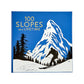 100 Slopes of A Lifetime" by Graphic Image features a skier silhouette amid snowy mountains and pines in blue and white—a gorgeous tribute to must-see ski destinations for your ultimate bucket list.