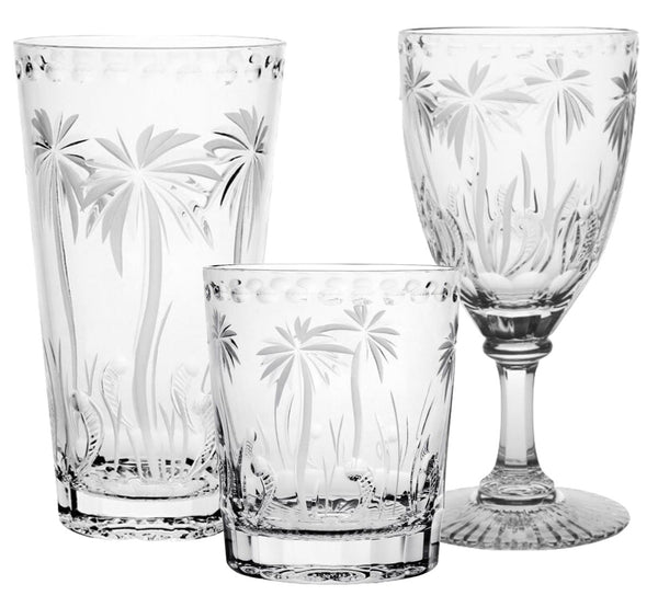 The William Yeoward Crystal Alexis Collection includes three handmade crystal pieces featuring a palm tree design: a tall cylindrical glass, a short tumbler, and a goblet, all meticulously hand-cut.