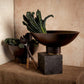 Two dark bowls from the Alhambra Bowl Collection by L’Objet, filled with kale and paired with wooden utensils and a black block, accent a brown tablecloth—recalling the charm of Alhambra Gardens.