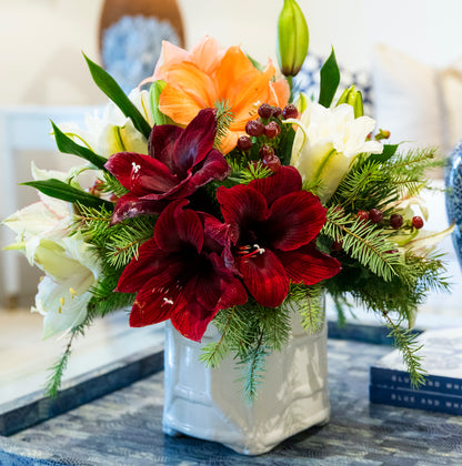 The Live Amaryllis Holiday Floral Arrangement by Hive Floral Studio features lush greenery and vibrant blooms in a ceramic vase, perfect as an indoor table centerpiece.
