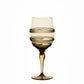 A yellow-tinted wine glass from Juliska’s Ella Drinkware Collection features a graceful spiral decorative pattern around the bowl and is set against a plain white background. This exquisite piece of mouth-blown glassware showcases the collection’s artisanal craftsmanship, blending elegance and handcrafted charm for any sophisticated table setting.
