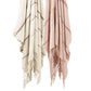 Two Matouk Amelia Stripe Throw Collection blankets—one beige with brown stripes, one pink with red—crafted from soft baby alpaca, hang side by side against a white background, perfect as cozy travel wraps.