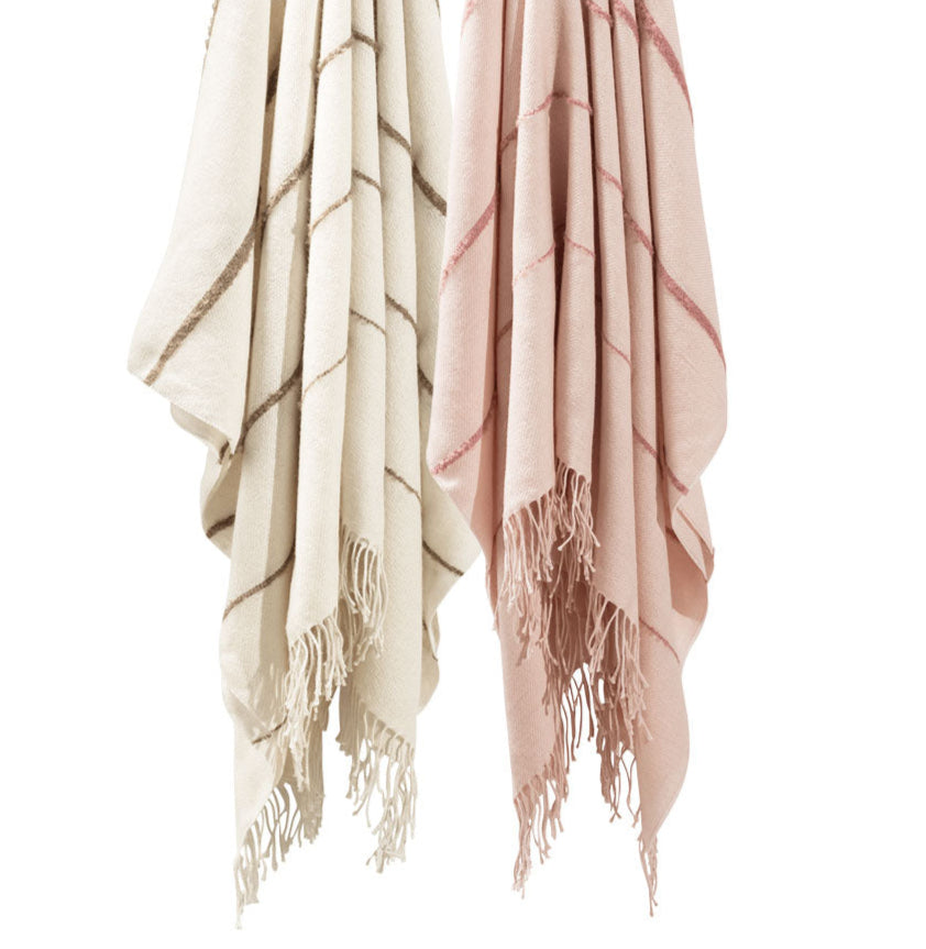 Two Matouk Amelia Stripe Throw Collection blankets—one beige with brown stripes, one pink with red—crafted from soft baby alpaca, hang side by side against a white background, perfect as cozy travel wraps.