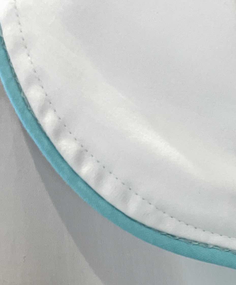Close-up of a white cotton sateen fabric edge with blue trim and visible stitching, highlighting the luxury sleep quality of the Haute Home Smart Pajama Pant Set.