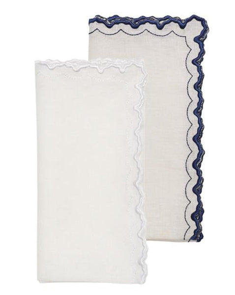 The Kim Seybert Arches Napkin Set includes two folded white linen napkins with scalloped edges: one with a dark blue embroidered geometric edge and another with a pristine white trim, offering versatile design.