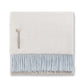 The Classic Herringbone Throw Collection by Alicia Adams Alpaca features a folded cream alpaca blanket with a tag and light blue fringe, fair-trade crafted in Peru, shown on a white background.