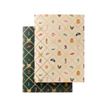 Two Holiday Argyle Pocket Notebooks: one dark green with a gold lattice, and one cream with a gold lattice and assorted holiday icons.