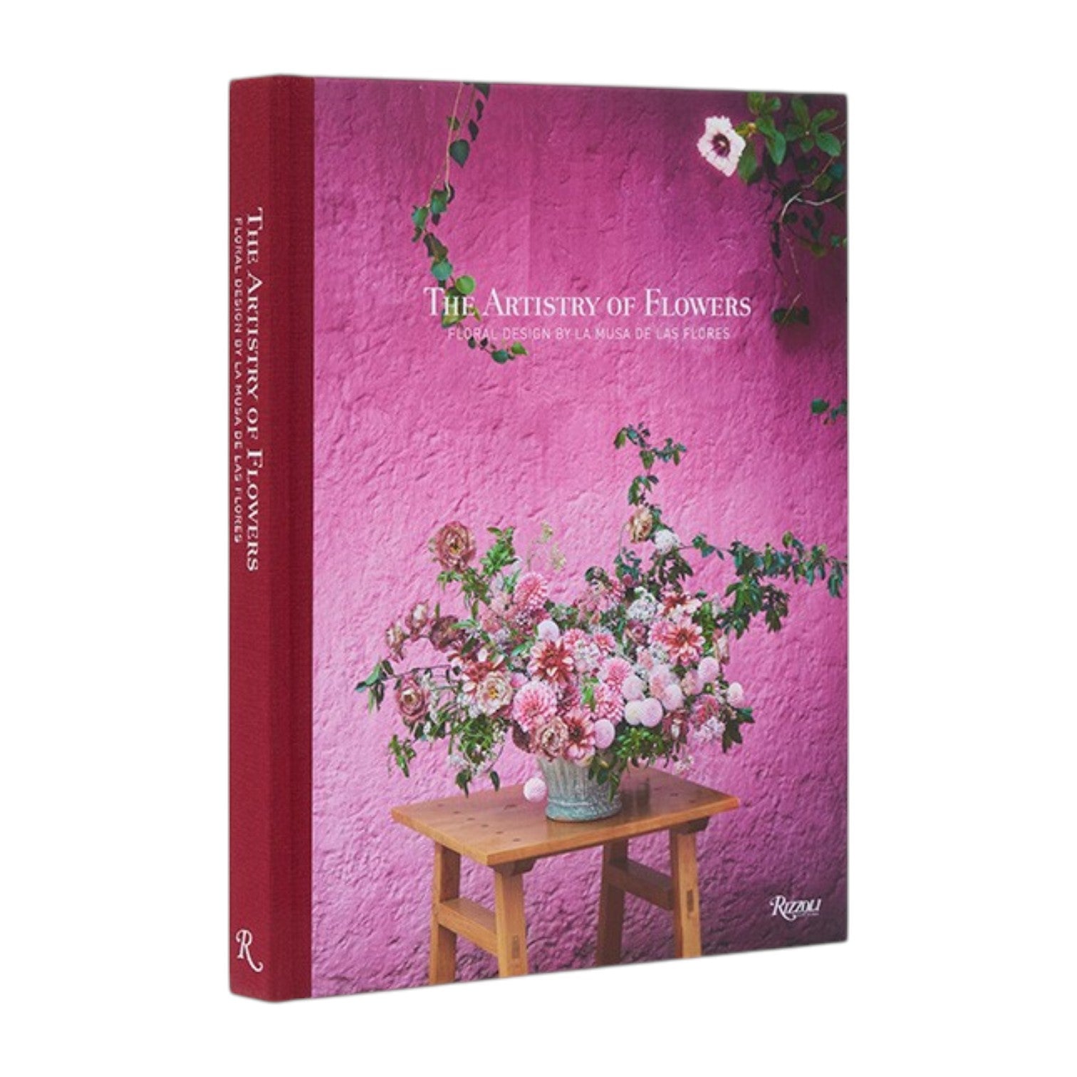 The Rizzoli book “The Artistry of Flowers” stands upright against a pink wall, its cover showcasing a floral arrangement atop a wooden table—an inspiring homage to the creativity of floral designers and indoor plant enthusiasts.
