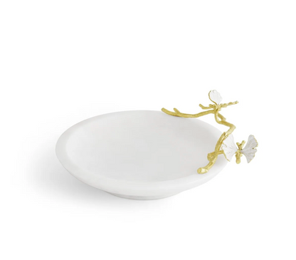 The Michael Aram Butterfly Ginkgo Gold Trinket Dish is a white, round luxury vanity dish featuring a gold branch and two butterfly accents on the rim.