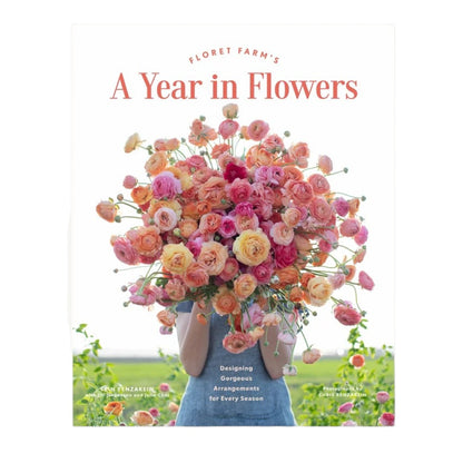 A person holds a large bouquet of pink and orange flowers in front of their face, showcasing the stunning floral design featured on the cover of “A Year in Flowers” by Chronicle Books.