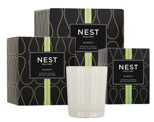 Three Nest Bamboo Candle Collection black and green boxes stand behind a white glass candle container featuring the Nest logo.