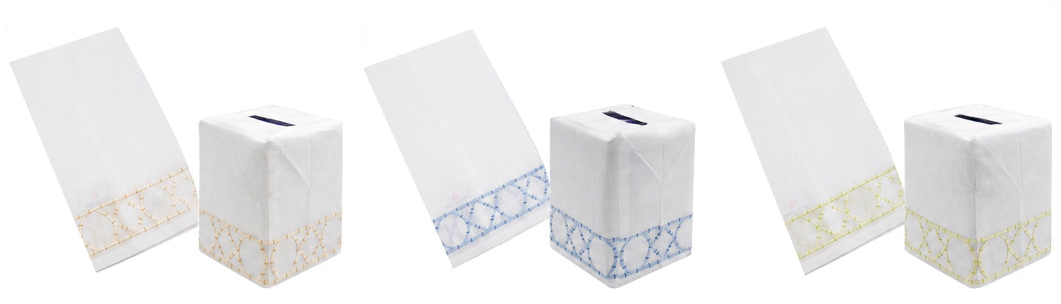 Four white Italian linen tissue box covers and matching hand towels from the Bamboozle Bath Collection by Haute Home—available in tan, blue, and green—each featuring a geometric embroidered border. Displayed on a white background, these pieces are perfect for elevating your home décor with timeless elegance.