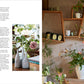 The left page of The Artistry of Flowers by Rizzoli features text alongside a photo of pink flowers arranged in petite vases, showcasing the creative skill of a floral designer; on the right page, a wooden shelf displays teapots, tea tins, cups, and a delightful floral arrangement in a white pitcher—offering perfect inspiration for indoor flowering plant enthusiasts.