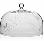 The Jasmine Cake Dome by William Yeoward Crystal is a clear glass dome with a round knob handle and an etched leafy branch design, showcasing handmade artistry and timeless elegance as part of the Jasmine Glassware Collection.