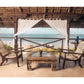 A covered open-air Beach House terrace with two wooden chairs and a glass-topped table, offering barefoot luxury with views of the beach and ocean.