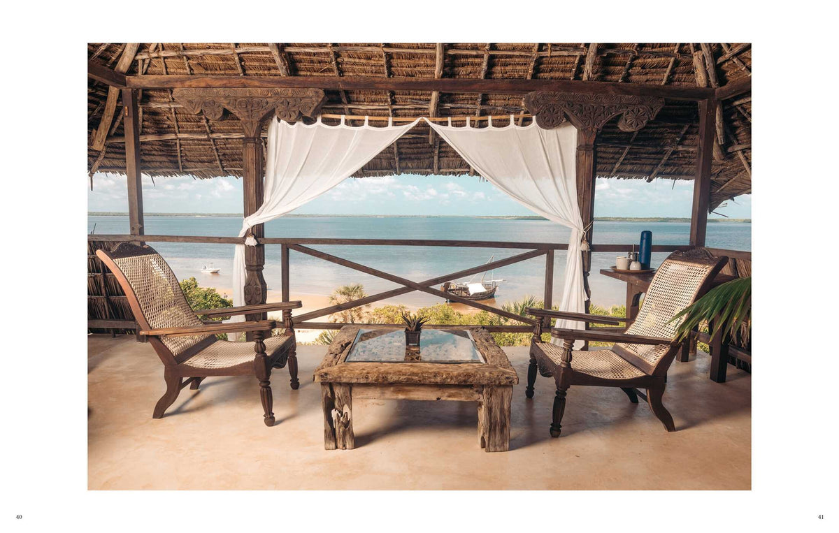 A covered open-air Beach House terrace with two wooden chairs and a glass-topped table, offering barefoot luxury with views of the beach and ocean.