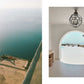 A person enjoys barefoot luxury, sunbathing on a Beach House cliffside ledge next to an arched doorway framing a coastal patio and the ocean.