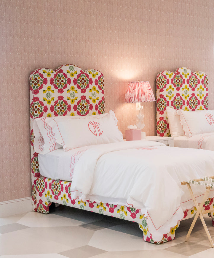 Two EJ Schrader Rosa Spring Twin XL Beds with floral headboards and white bedding sit side by side in a pink-walled bedroom, complemented by playful furniture, a nightstand, and a lamp between them.