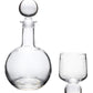 The Simon Pearce Benson Drinkware Collection features a clear glass decanter with a round stopper beside a short, round glass on a white background, highlighting clean lines inspired by Bauhaus architecture.