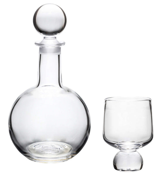 The Simon Pearce Benson Collection, featuring a clear glass decanter with a round stopper and an empty goblet beside it, captures the Bauhaus spirit by merging form and function into a geometric statement.