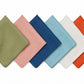 Six square linen napkins from the Juliska Berry Scallop Napkin & Tablecloth Collection are arranged in a row, each showcasing a different color—green, pink, blue, light blue, white, and orange—against a crisp white background. These finely woven pieces pair beautifully with matching or contrasting linens from the collection to create an inviting table setting.