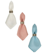 The Berry Scallop Napkin Set by Juliska features three linen napkins in white, pink, and blue with silver rings. Expertly woven in Portugal, they add elegance to any table.