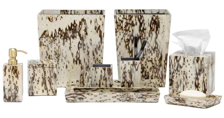 The Pigeon & Poodle Bisbee Bath Collection features a cream and brown speckled pattern, including a soap dispenser, waste bin, tissue box cover, toothbrush holder, and trays with nature-inspired accents.