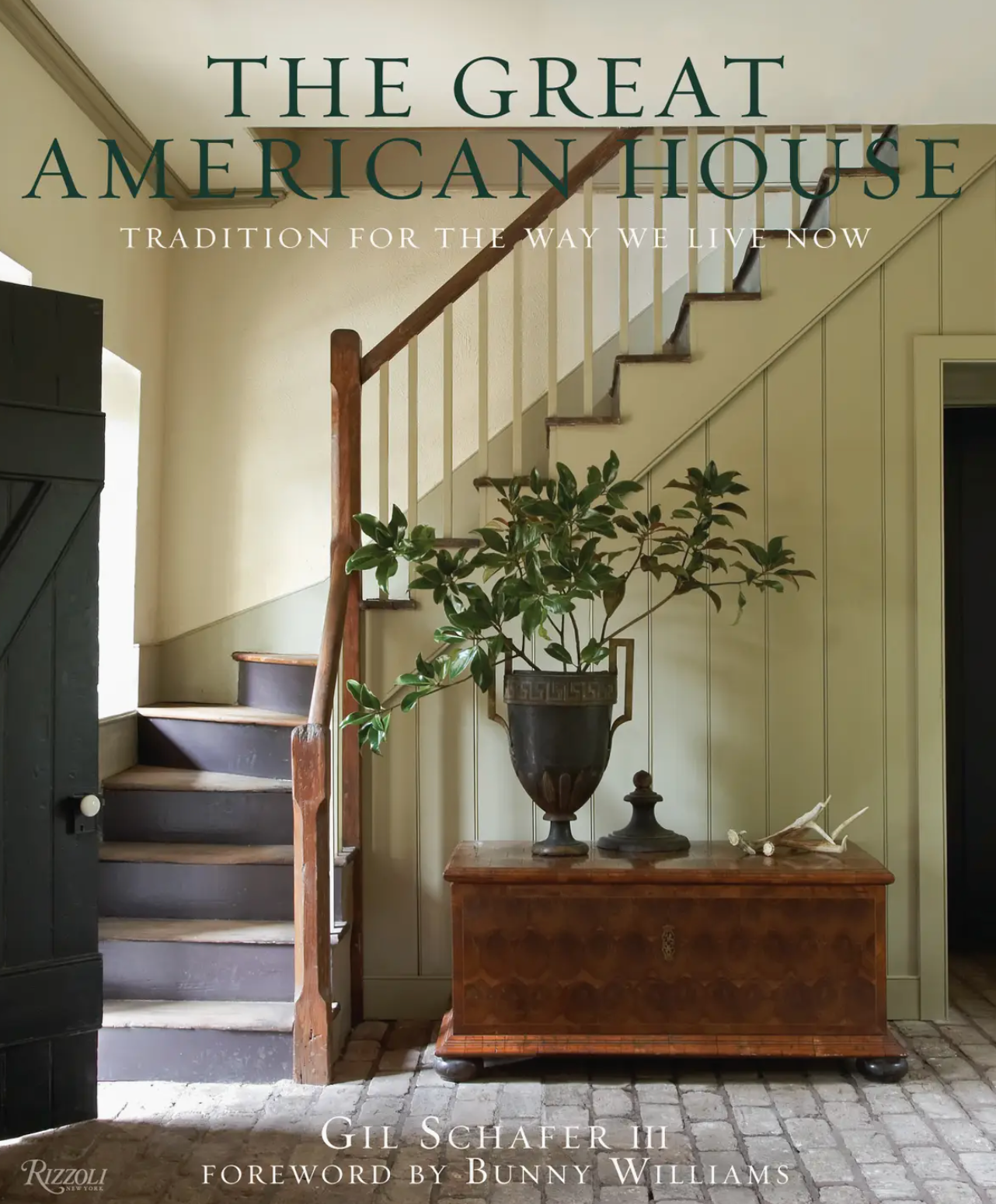 The cover of The Great American House by Rizzoli features a hallway with a wooden staircase, a chest topped with a vase of greenery, and the title by Gil Schafer III, beautifully capturing the timeless elegance of classical architecture.