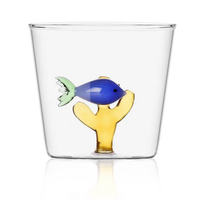 From the Marine Garden Drinkware Collection by Ichendorf Milano, this clear glass tumbler features a decorative blue handmade glass fish and yellow coral at its base.