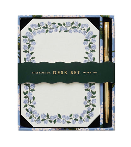 The Blue Hydrangea Desk Accessory Collection by Riffle Paper Co. includes a floral-bordered notepad and gold pen, making it the perfect addition to any workspace.