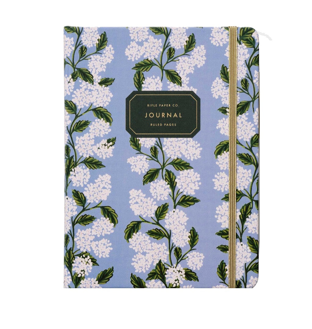 Part of the Rifle Paper Co. Blue Hydrangea Stationery Collection, this blue hardcover journal features a white floral design, a gold elastic closure, and a black "Journal" label on the front cover.