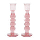 The Juliska Provence Candlestick Set by Juliska features two pink, mouth-blown glass holders with a bulbous, tiered design, shown side by side on a white background for a vibrant accent in any space.