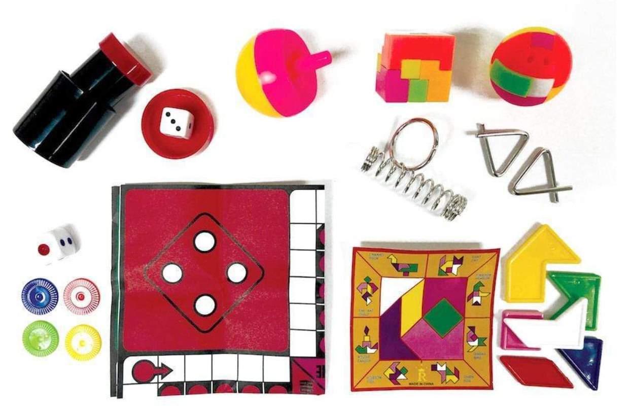 A vibrant array of board game pieces, dice, cards, puzzle shapes, tokens, a spinning top, a spring, and metal puzzles are artfully arranged on a white background—making the Caspari Party Hats Celebration Cracker Set an ideal choice for holiday party favors or festive gatherings.