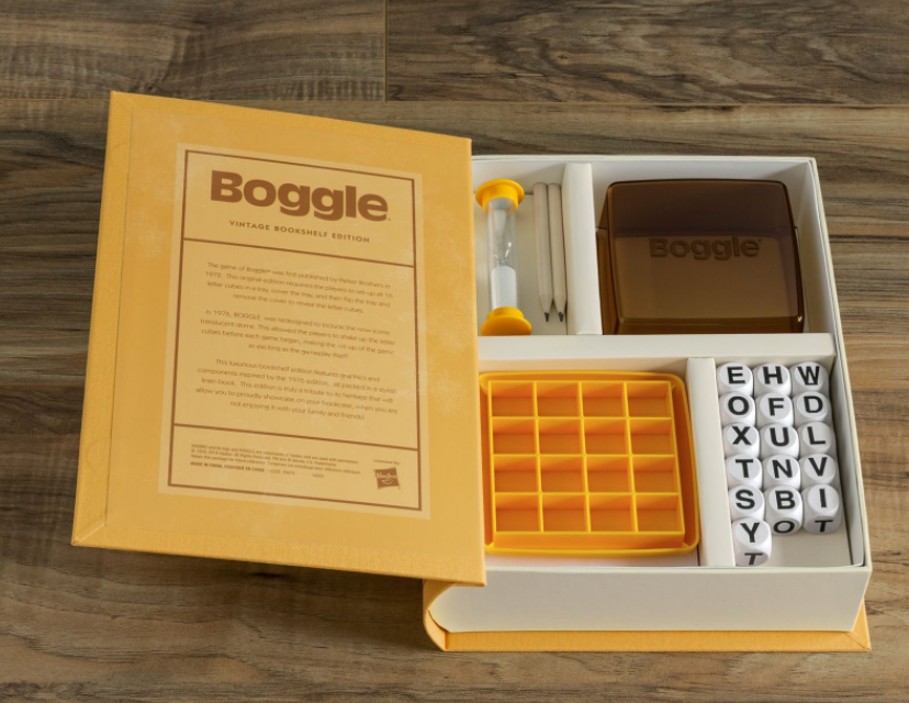An open Boggle game set displaying letter cubes, an hourglass, a notepad with two pencils, and a storage tray. The game is labeled "Boggle Vintage Bookshelf Edition" by WS Game Company, reminiscent of the classic 1976 edition.