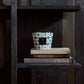 A ceramic mug and two stacked books titled "Johannes Dahlem" and "China," next to a Baobab Collection Bohomania Kilan candle on a shelf in a dark wooden bookcase.