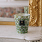 A Baobab Collection Bohomania Lazlo scented candle in a cut glass holder placed on a white marble mantel, with a gilded mirror and ornate decor in the background.