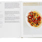 An open Phaidon Home Farm Cooking cookbook from the Phaidon recipe collection displaying a recipe on the left page and a colorful plated dish on the right, likely the completed recipe from the cookbook.