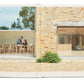 Two individuals engaged in conversation about their recipe collection while seated at an outdoor table, as seen in a photograph within an open Phaidon Home Farm Cooking book.