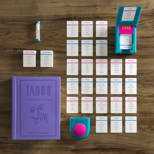 A photograph of the WS Game Company's Taboo Vintage Bookshelf Edition reveals its components neatly arranged on a wooden surface. The items include a sand timer, a deck of cards in a card holder, a purple game manual, and a buzzer.