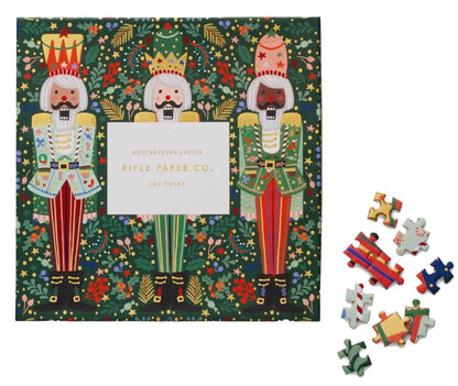 A box of Riffle Paper Co.'s Nutcracker Brigade Puzzle, showing three illustrated nutcrackers on the cover, with several loose puzzle pieces beside it.