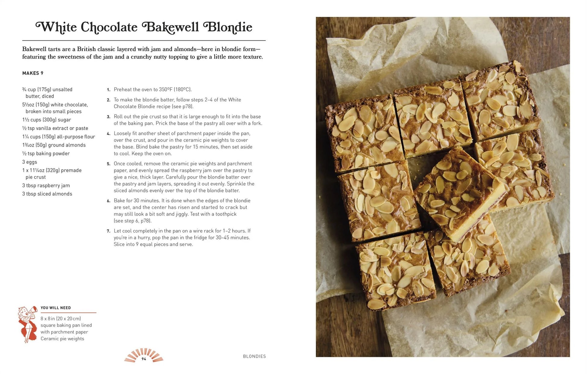 A tray of white chocolate bakewell blondies—taking inspiration from delicious recipes featured in *The Brownie Book by Kate Jenkins* from Penguin Random House—is cut into squares and topped with flaked almonds. The blondies rest on parchment paper atop a rustic wooden surface.