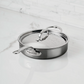 A Hestan NanoBond Covered Sauté pan sits on a white marble countertop against a white tiled backsplash.