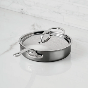 A Hestan NanoBond Covered Sauté pan sits on a white marble countertop against a white tiled backsplash.