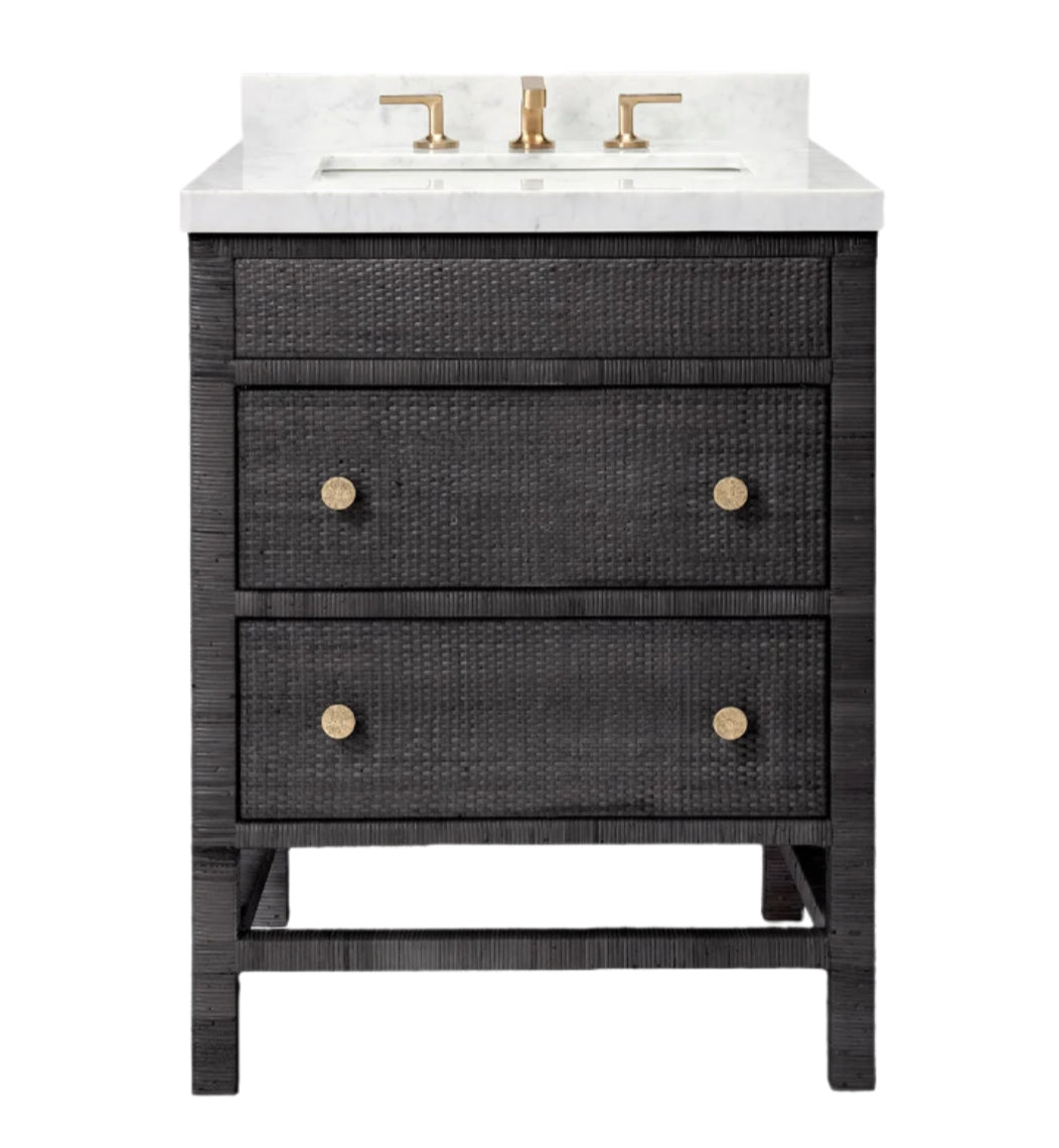 The Isla Vanity Collection by Made Goods is a freestanding bathroom vanity with a black finish, two drawers, gold knobs, a white countertop, an under-mount sink, and elegant gold faucet fixtures.