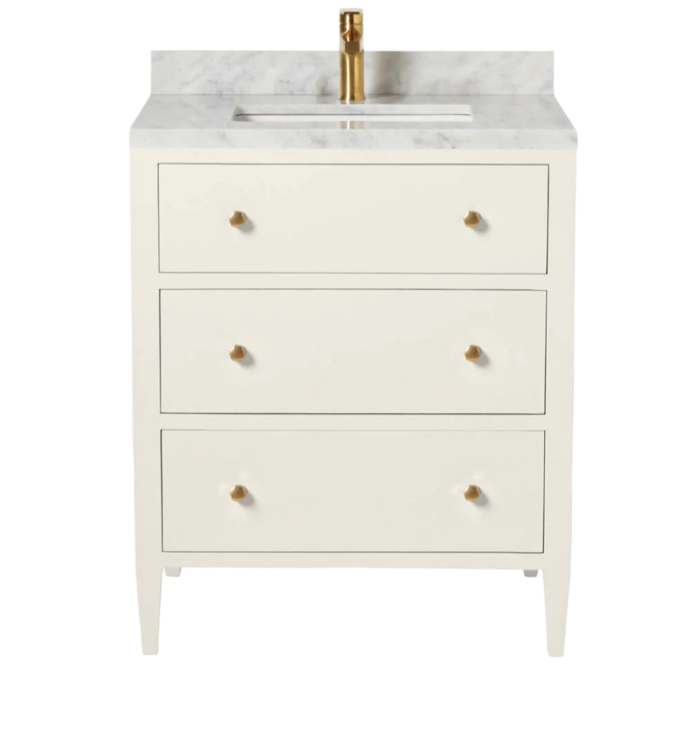 The Jarin Vanity Collection by Made Goods features a white freestanding vanity with three drawers, brass handles, a marble countertop, and a brass faucet—an elegant addition to any bathroom.