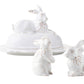 The Juliska Whitewash Bunny Serveware Collection features three white ceramic rabbit figurines: one resting on a butter dish and two upright as charming salt and pepper shakers, each adorned with subtle bow details.