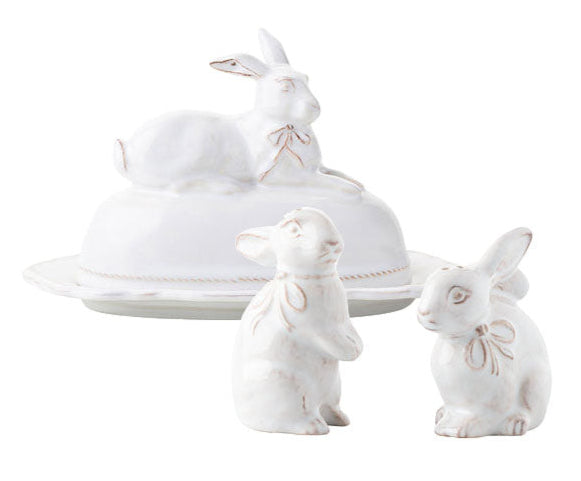 The Juliska Whitewash Bunny Serveware Collection by Juliska features a white ceramic butter dish with a bunny lid and two standing bunny salt and pepper shakers, all with delicate ribbon details.